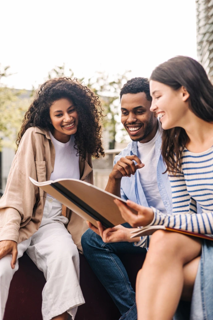 Étudiants souriants échangeant autour d'un livre à l'extérieur