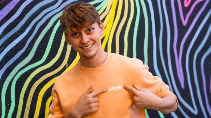 Étudiant souriant portant un sweat ESDAC devant une fresque murale colorée